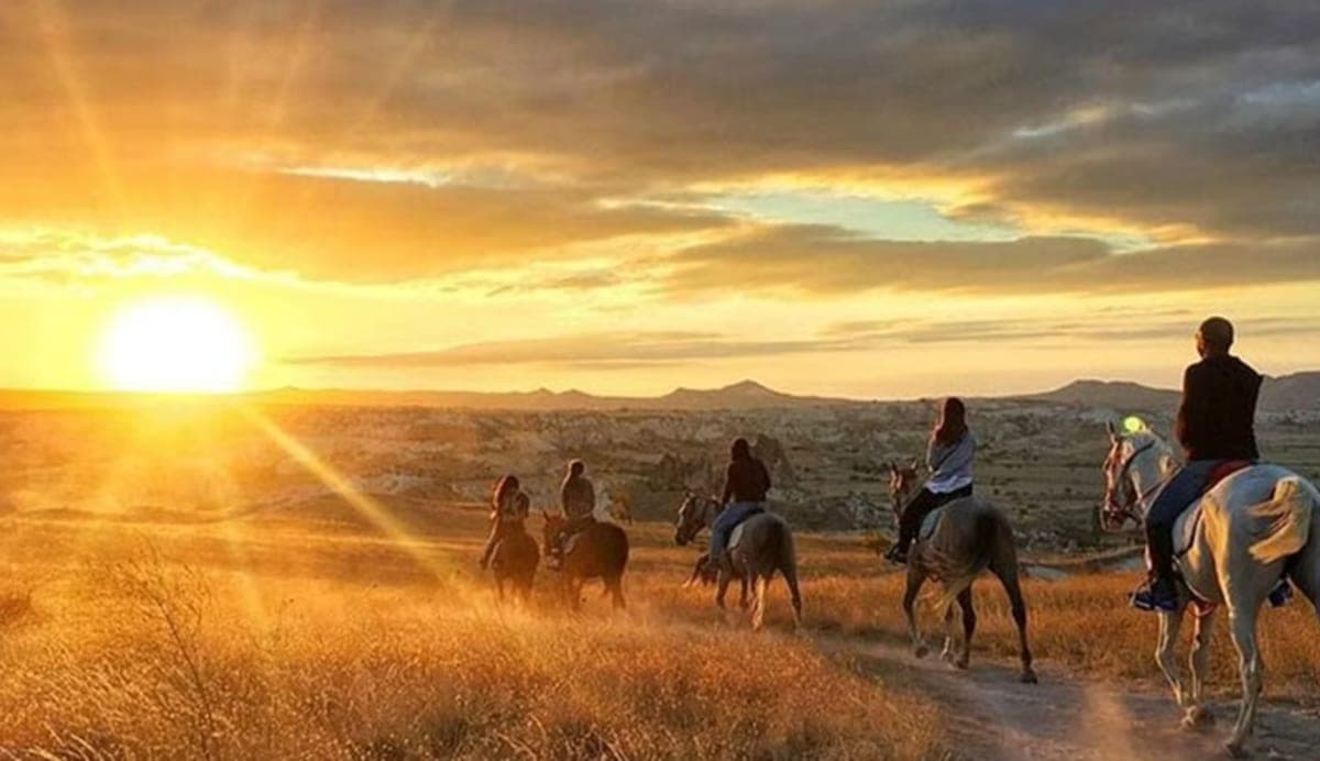 Riders in single file crossing open ground in Cappadocia at sunset
